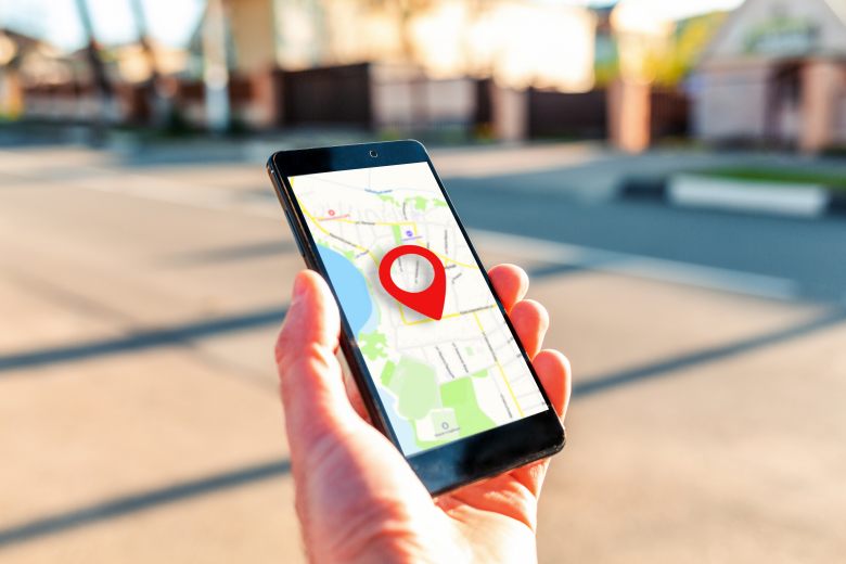 Male hand holding holding smartphone with online-a map on which the geolocation icon. In the background, a blurred street. Close up. Concept of online navigation and GPS.