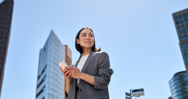 Young beautiful Asian business woman using smartphone on city street